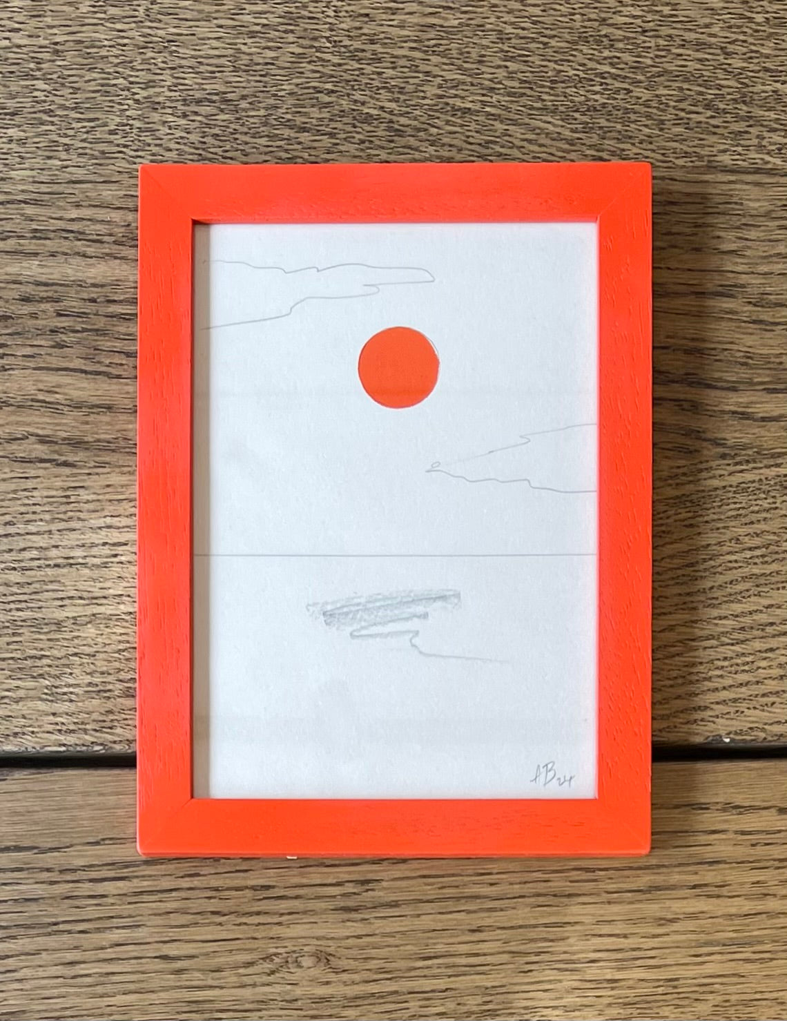 Framed artwork with a red circle on a white background, placed on a wooden surface.